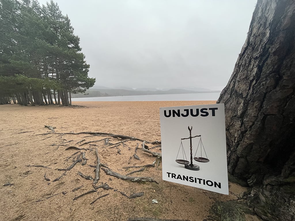 A sign saying: Unjust Transition stands against a scenic Cairngorms National Park backdrop.